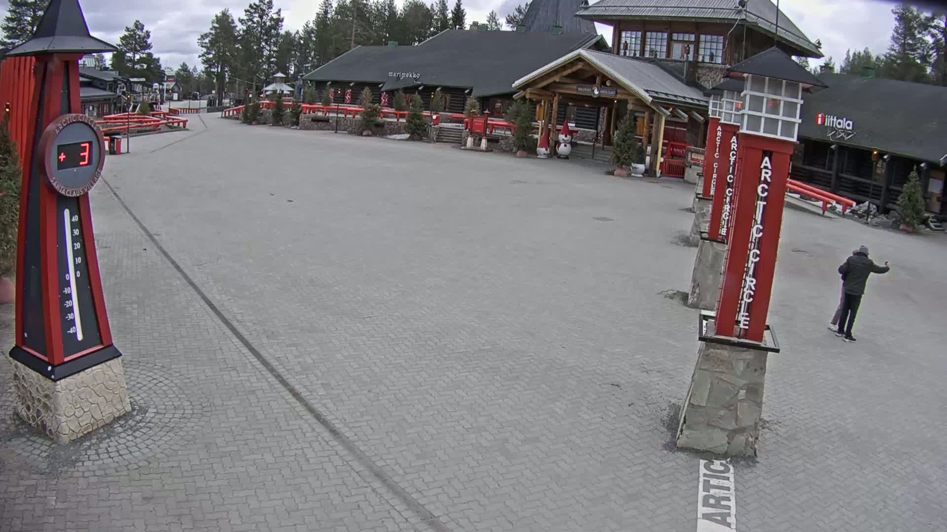 A paved plaza with several red and gray pillars and a log cabin-style building in the background under an overcast sky.
