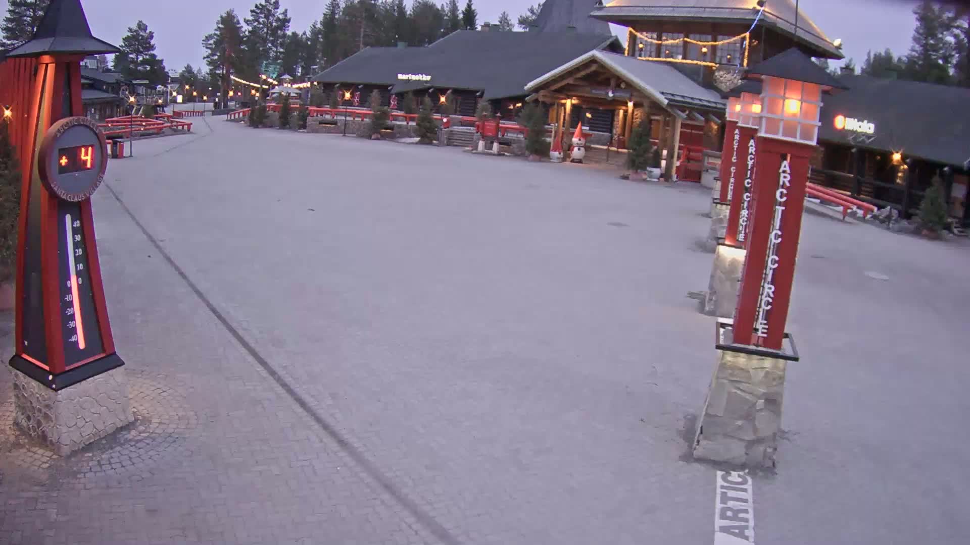A paved plaza with several buildings and illuminated red markers in the foreground, under a twilight sky.