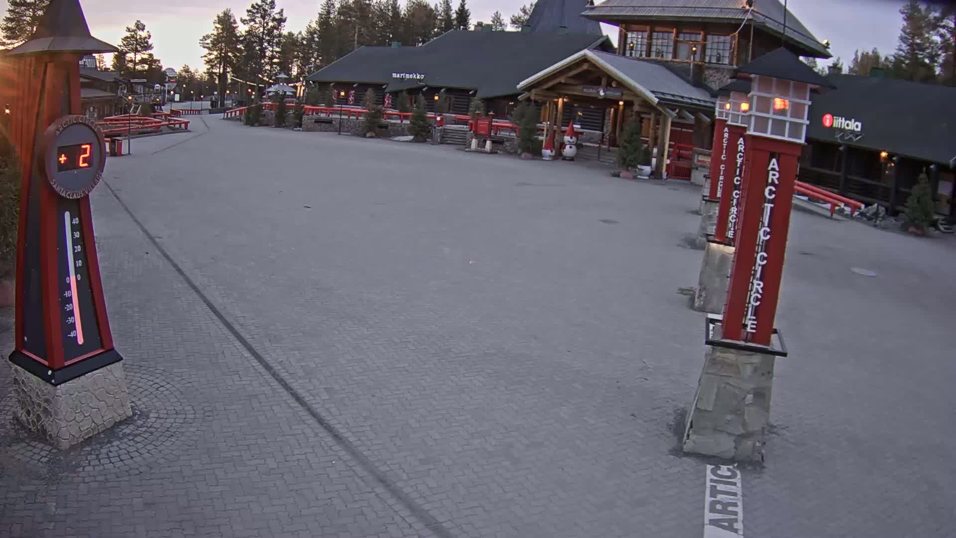 A paved plaza with several log buildings in the background, under a twilight sky, shows a temperature of 2 degrees.