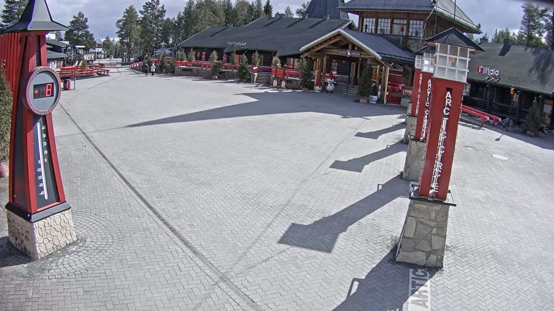 A paved plaza with several tall, red signposts and a large log cabin-style building under a sunny sky.