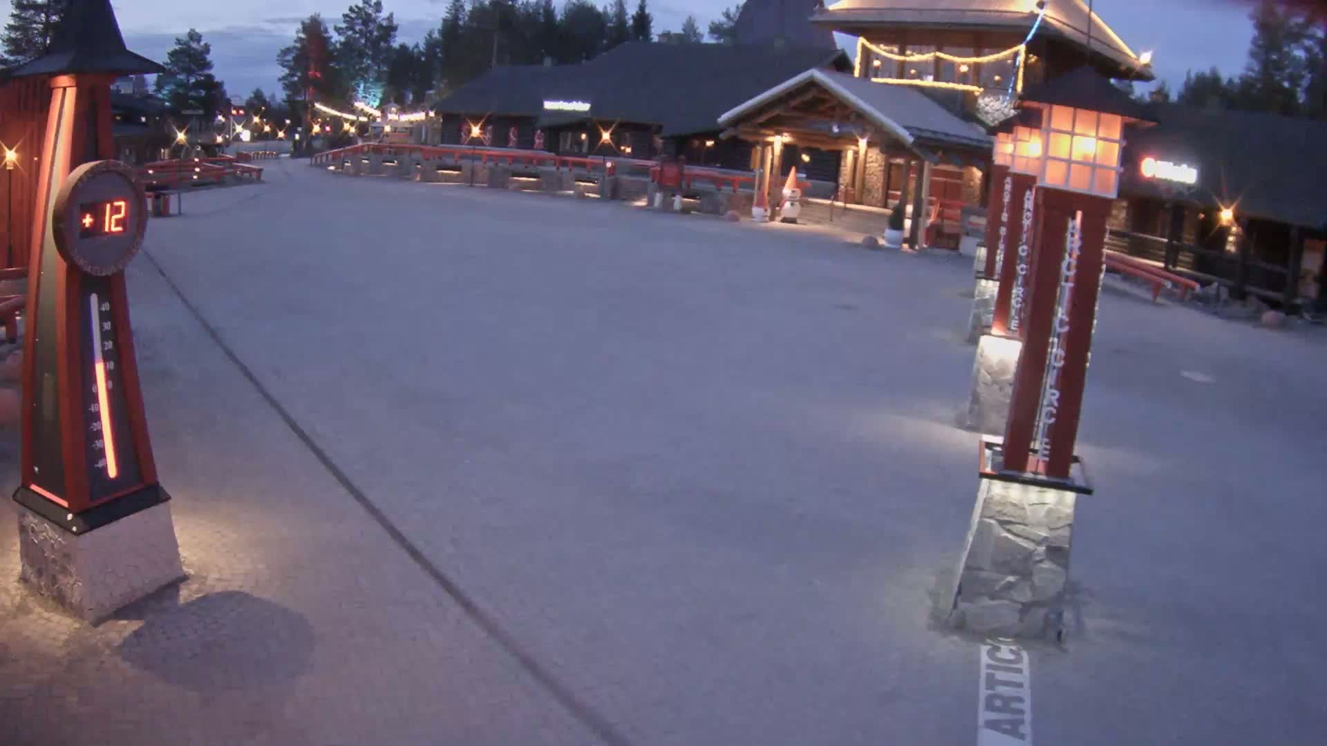 A paved plaza with illuminated lampposts and a digital thermometer displaying 12 degrees is visible under a twilight sky.