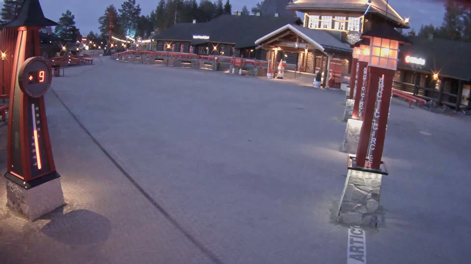 A paved area at dusk shows a thermometer reading 9 degrees, several illuminated lamp posts, and a building in the background.