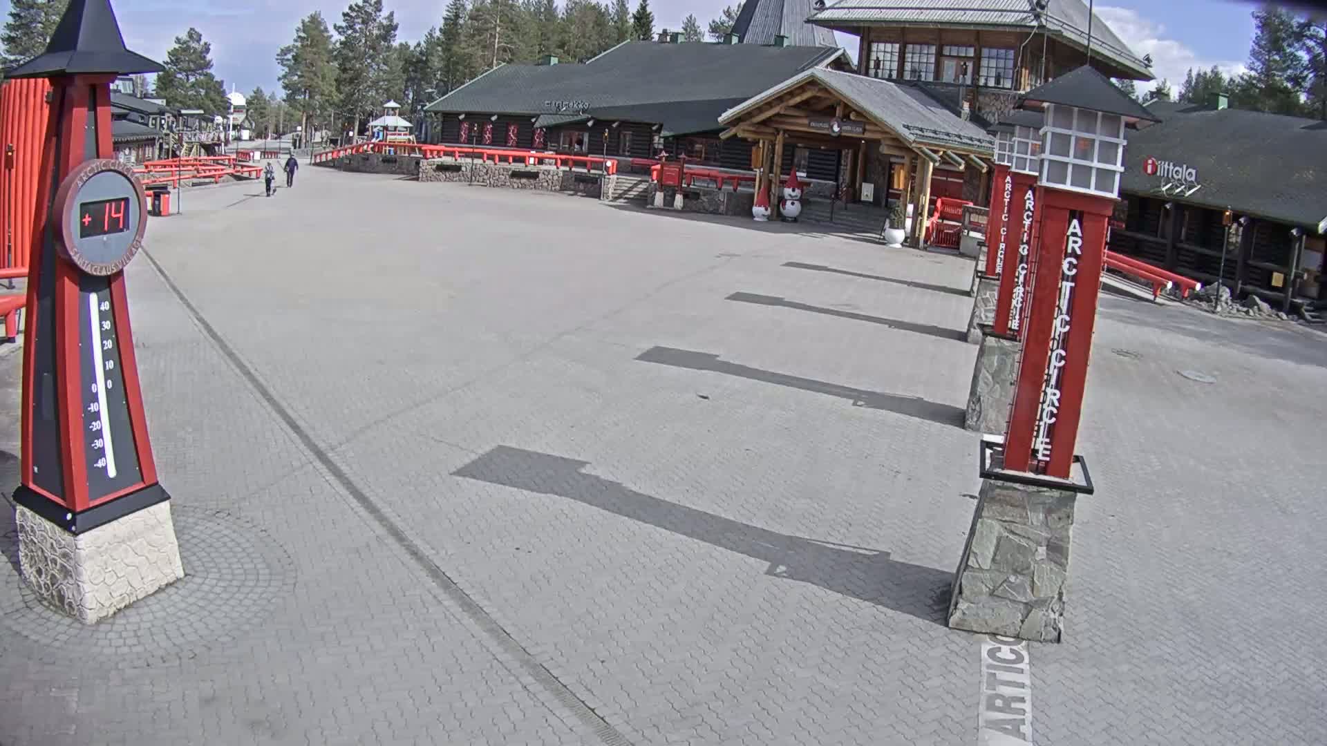 A paved plaza with several tall, slender red and black pillars stands in front of a log cabin-style building under a sunny sky.