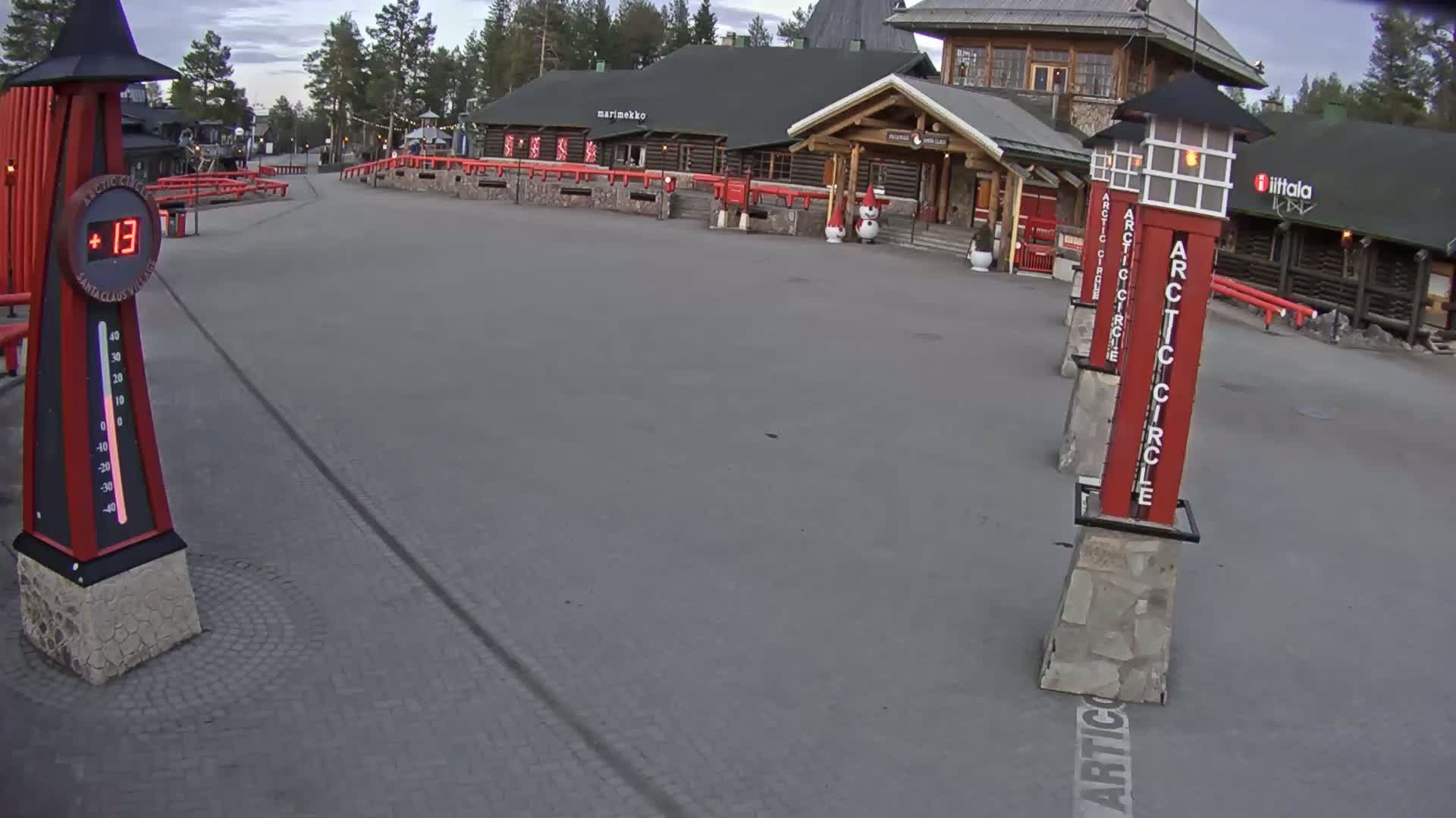 A paved plaza with several red and white Arctic Circle markers and a log cabin building in the background, under an overcast sky.