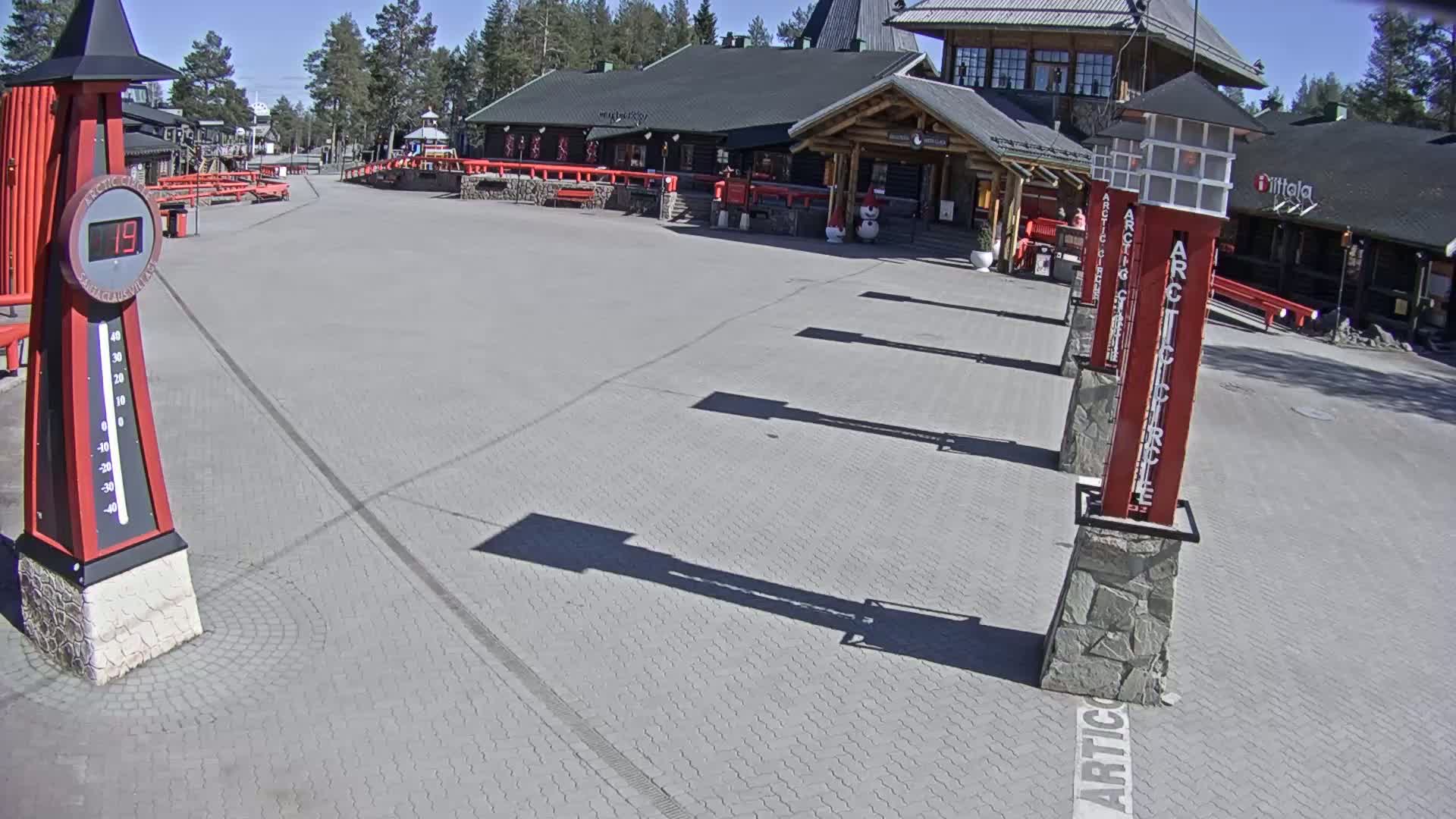 A paved plaza with several tall red markers and a large building in the background on a sunny day.