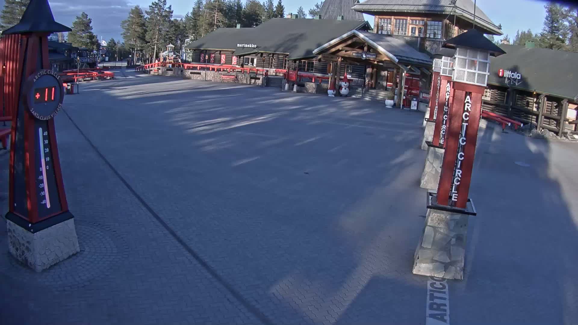 A paved plaza sits in front of several log buildings under a partly cloudy sky; a thermometer shows a temperature of 11 degrees.