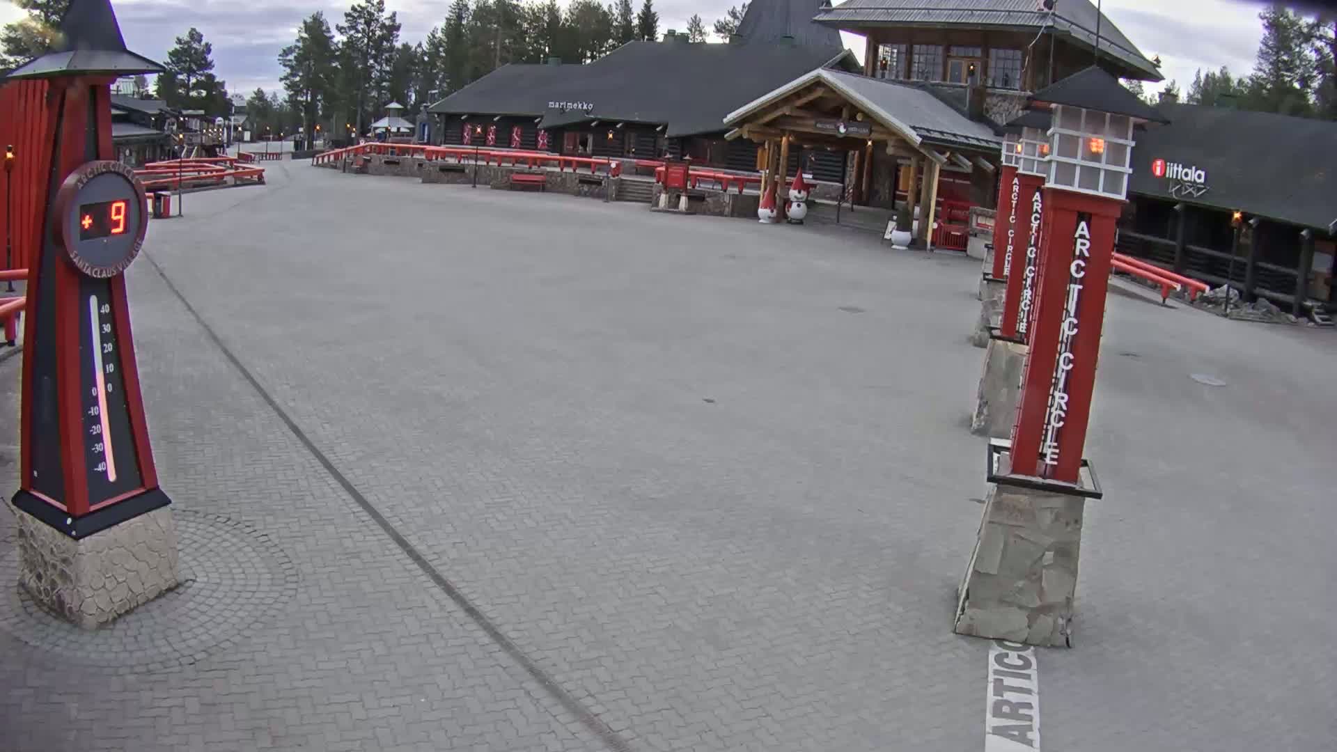 A paved plaza with several red Arctic Circle markers and a building in the background under an overcast sky, showing a temperature of 9 degrees.
