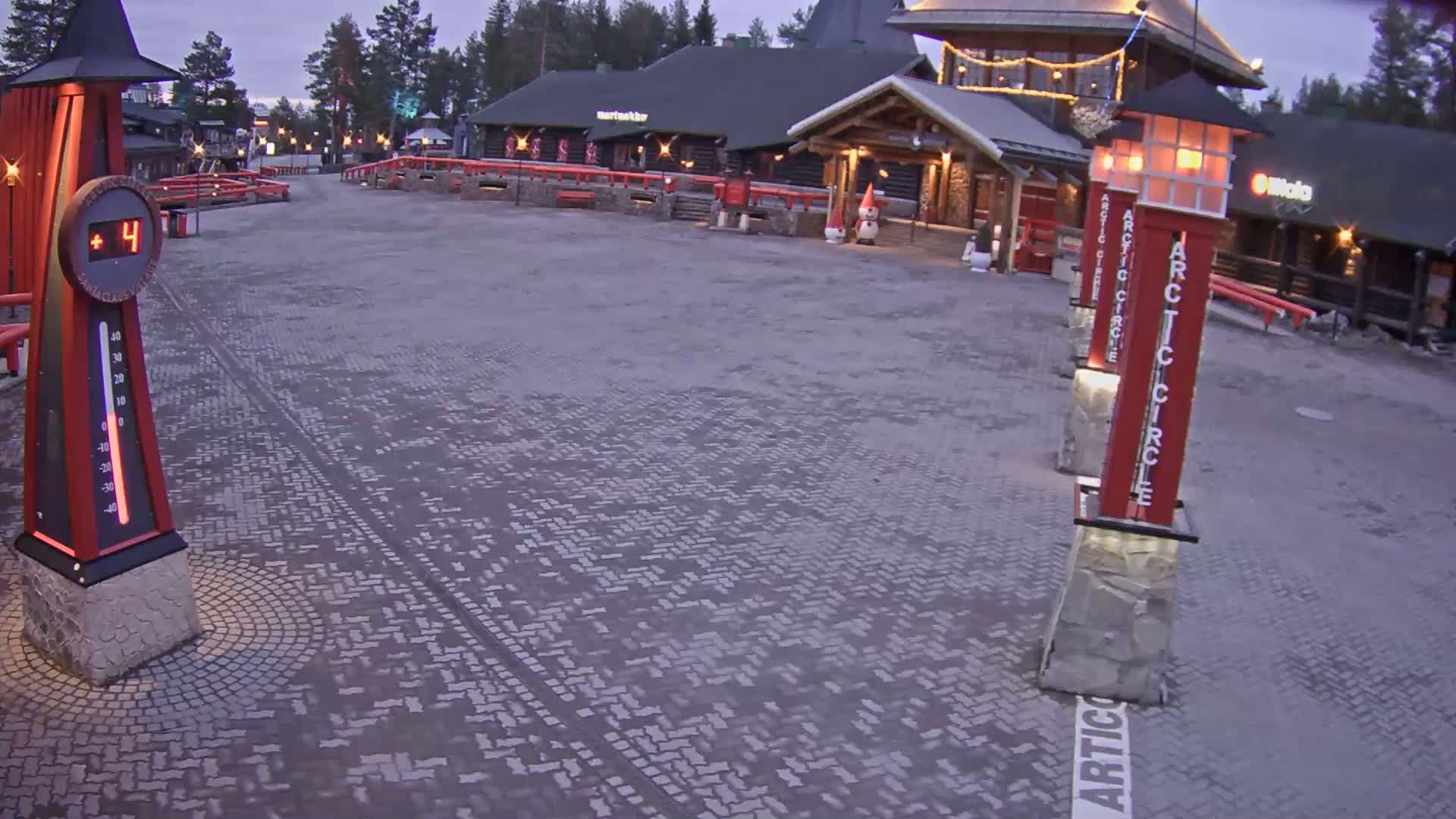 A paved plaza, showing a temperature of 4 degrees, is situated in front of several log buildings under a twilight sky.