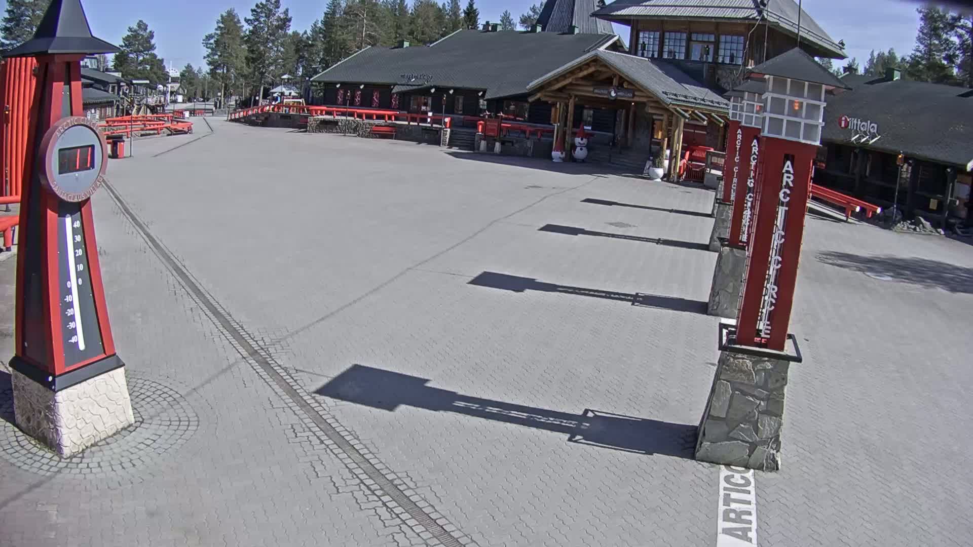 A paved plaza with several red and gray pillars and a large thermometer under a sunny sky.