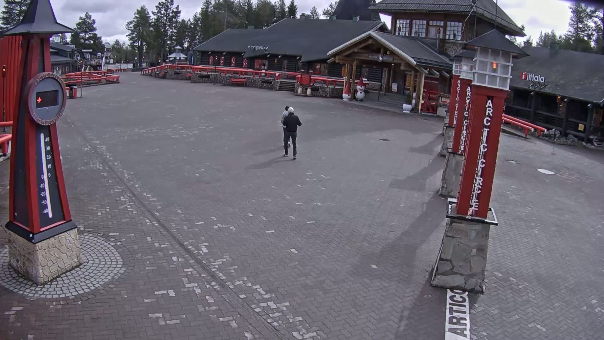 Two people walk across a brick plaza in front of a log building on an overcast day.