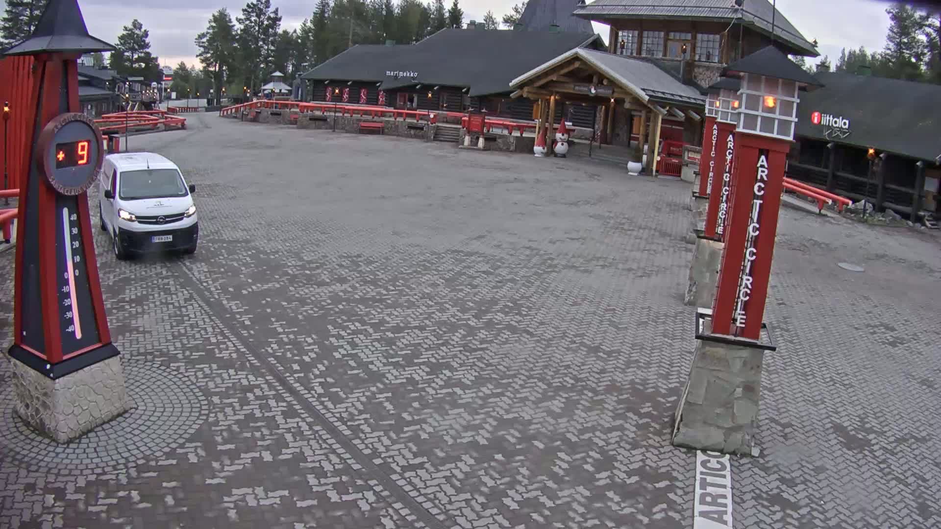 A white van is parked in a paved area in front of a log cabin building under an overcast sky.