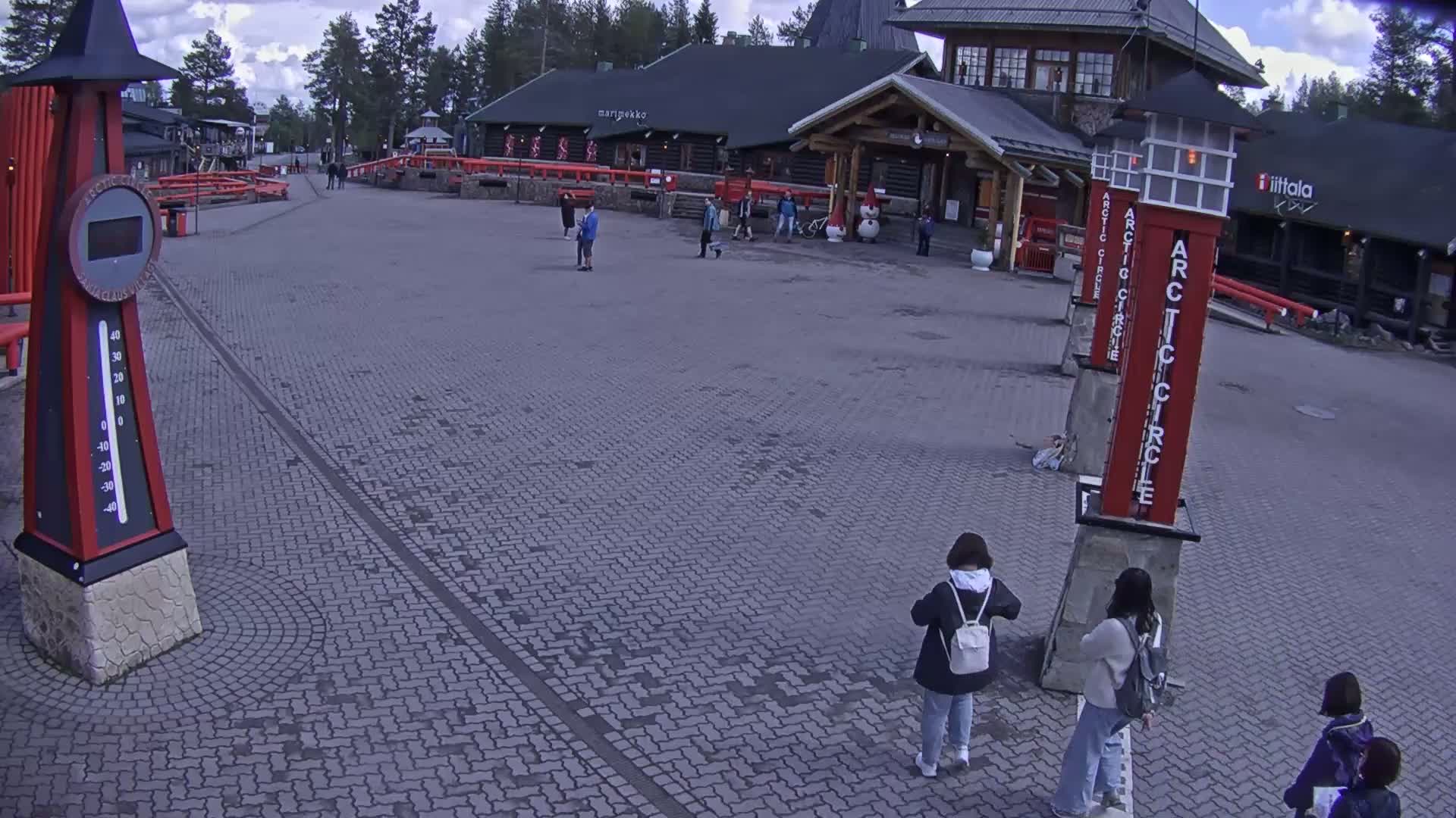 A brick paved plaza with several people walking near buildings on an overcast day.