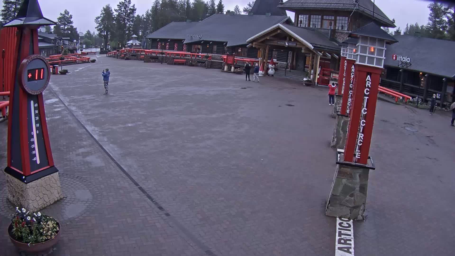 A paved plaza with several people, a large building, and tall red markers on an overcast day.