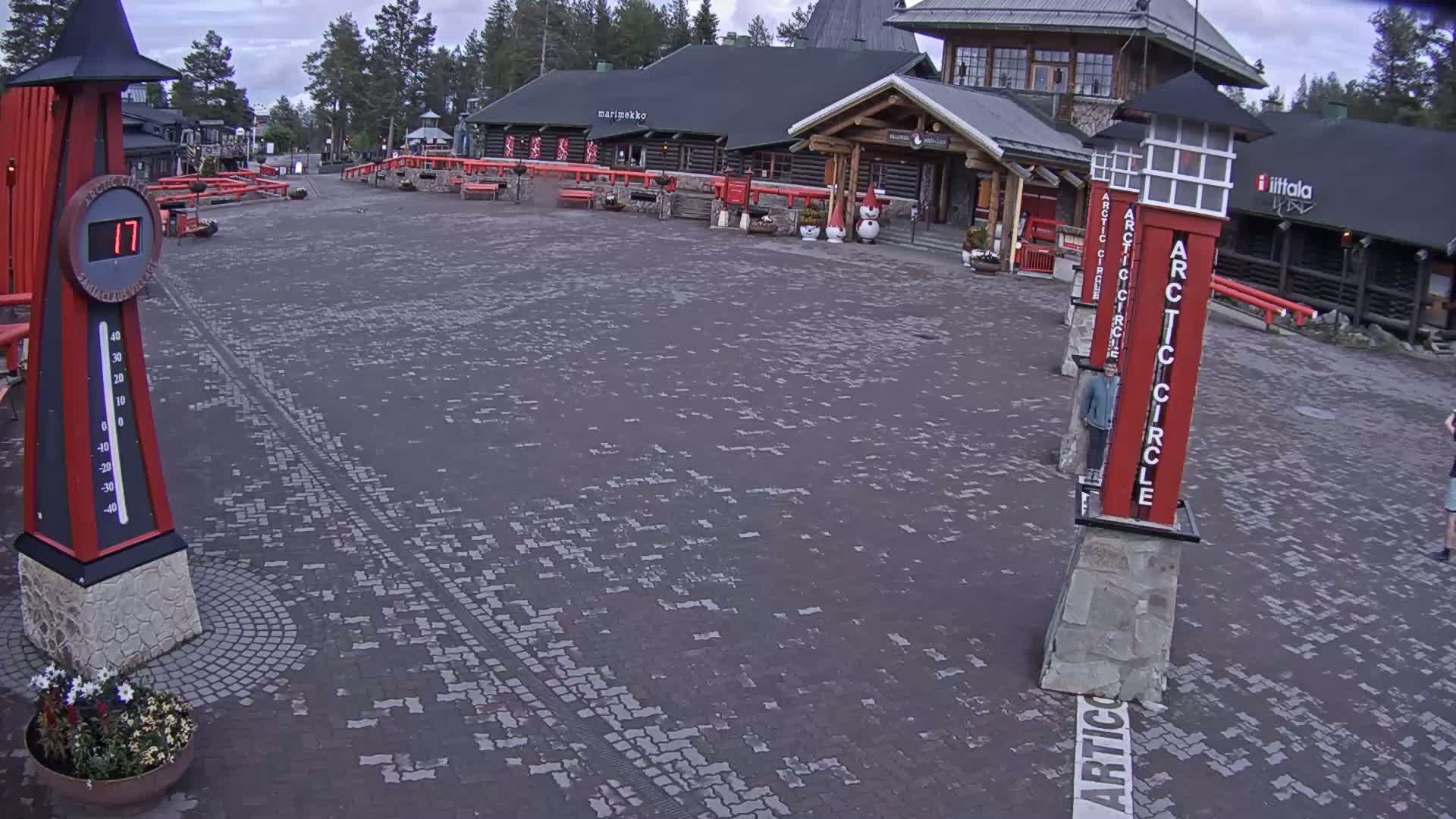A paved plaza with several buildings and tall, red, Arctic Circle markers is visible under an overcast sky.