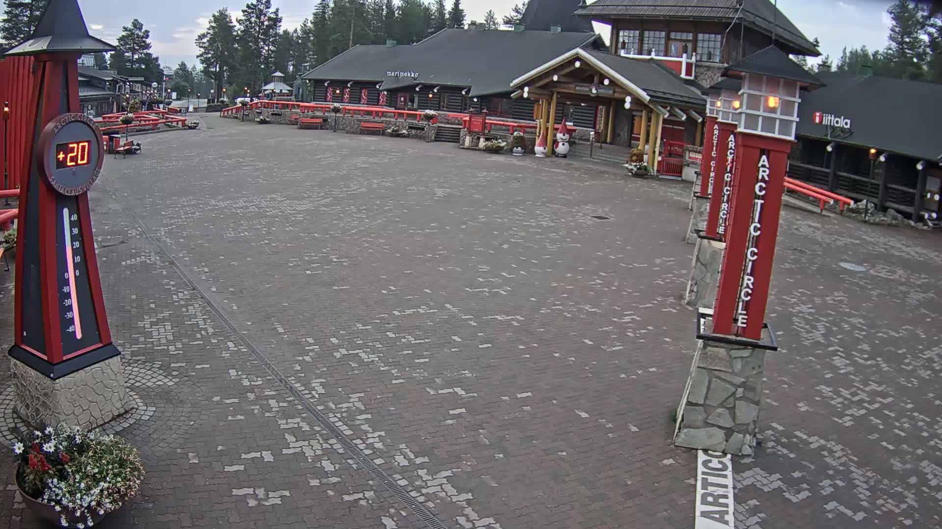 A paved plaza with a few people walking, near a building complex on a sunny day.