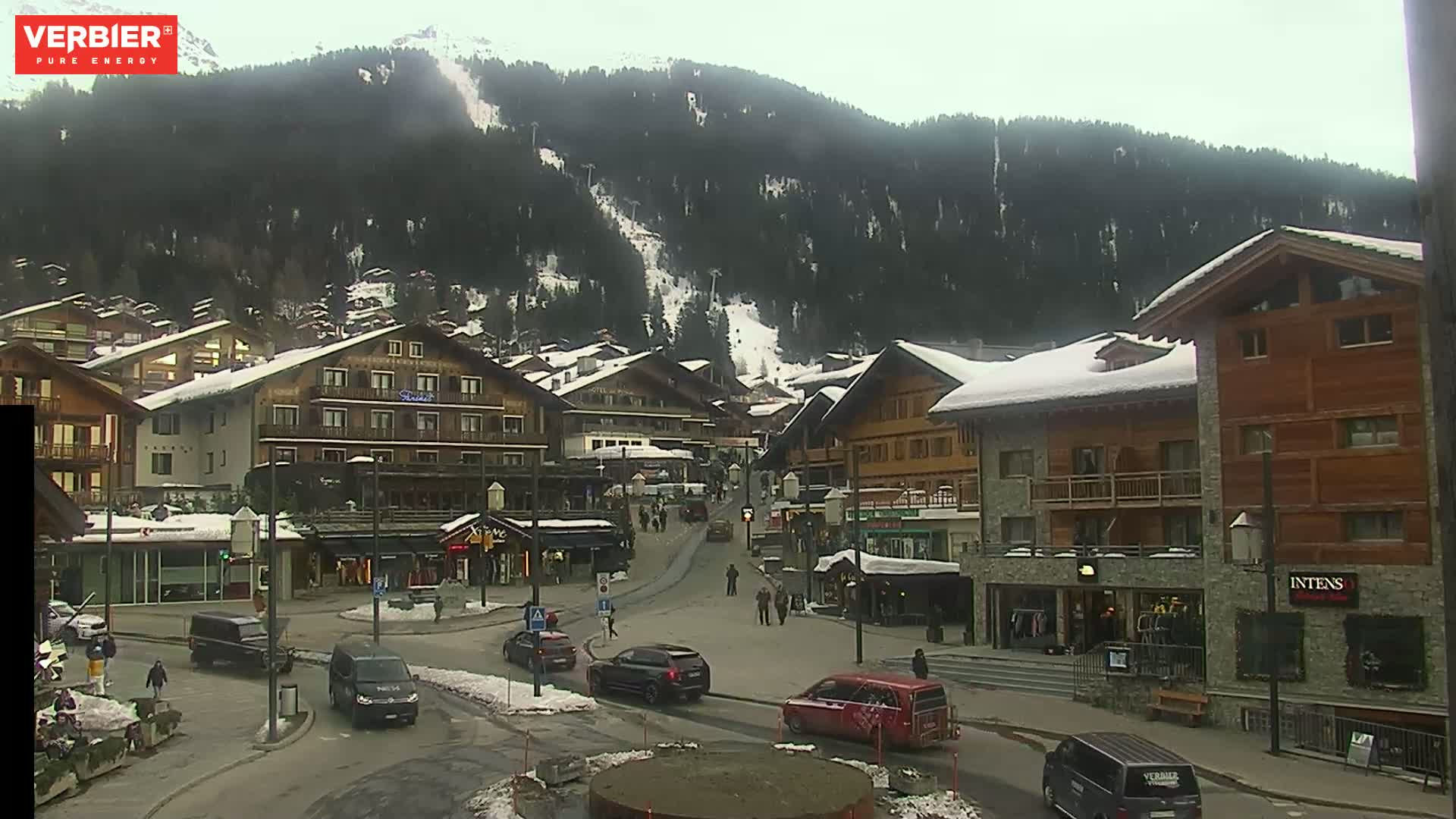 A snow-dusted village nestled at the base of a snow-covered mountain range on an overcast day.
