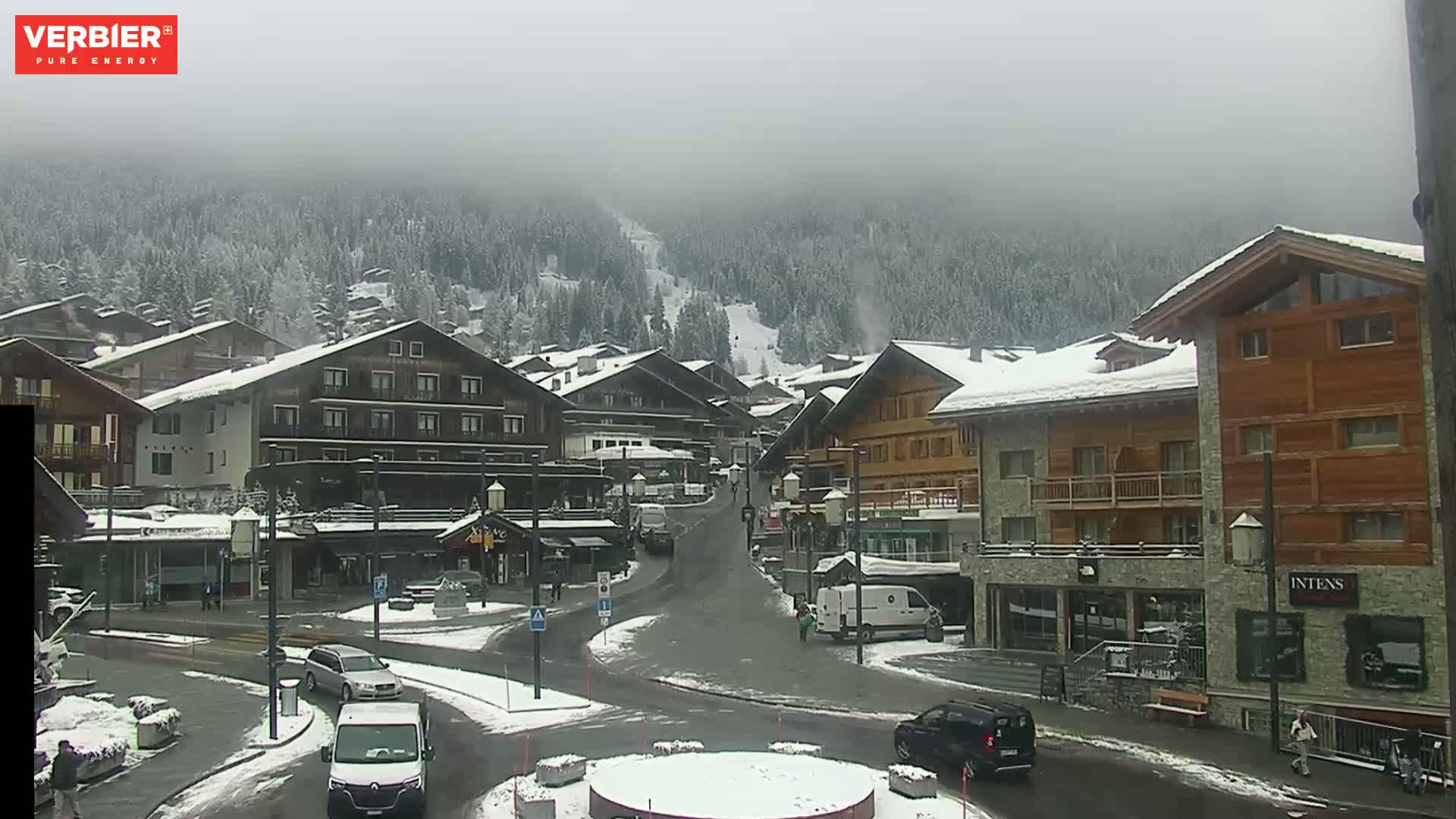 A snow-covered village nestled in a valley amongst snow-dusted mountains under a hazy sky.