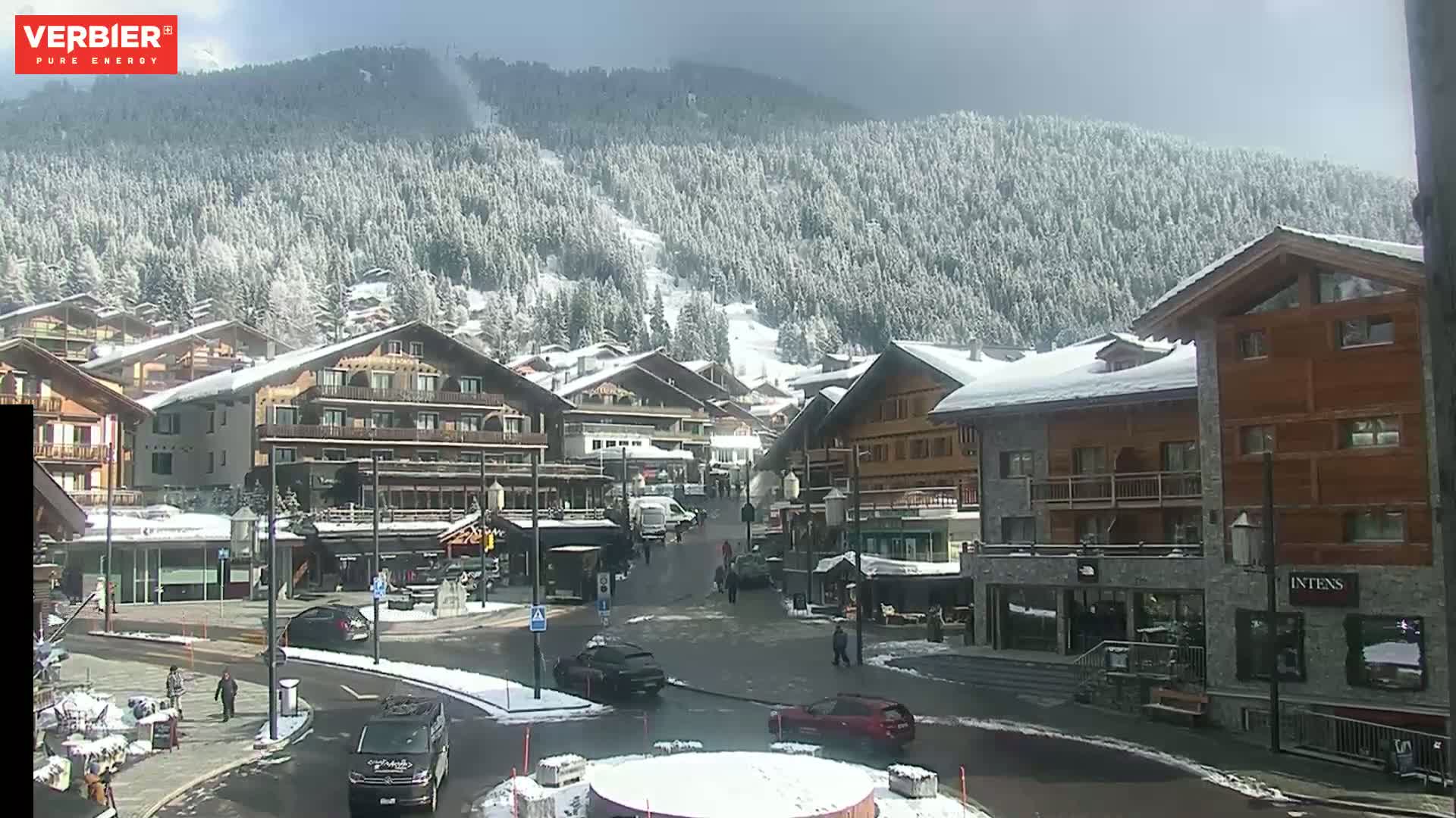 A snow-covered village nestled in a mountain valley under a partly sunny sky.