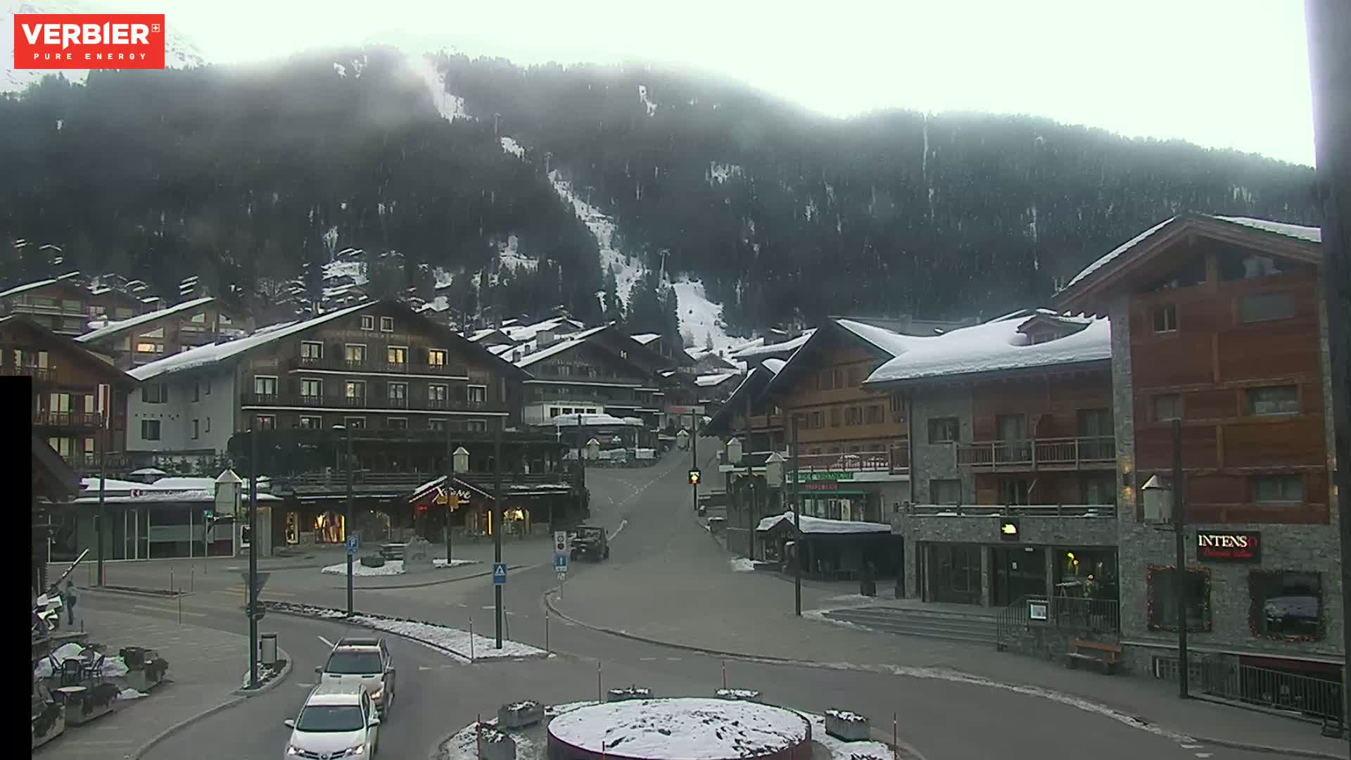 A snow-dusted village nestled in a valley surrounded by a misty, snow-capped mountain range.