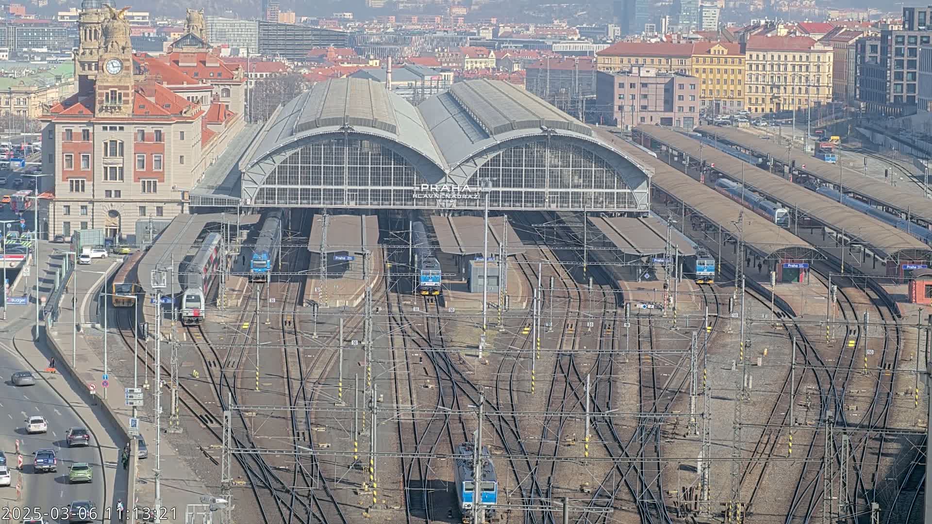 A large train station with many tracks and trains, surrounded by a city on a sunny day.