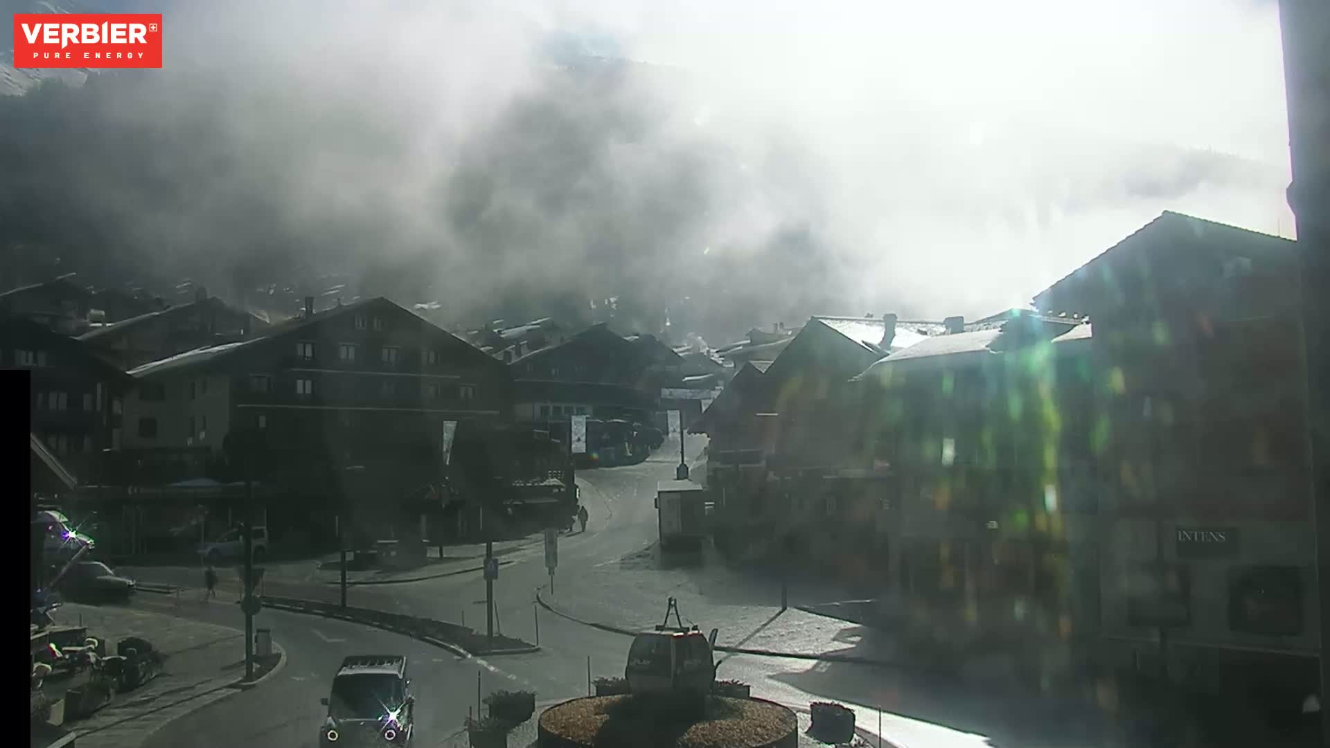 A foggy, sunny day in a town with several buildings, a road, and a small cable car in a roundabout.