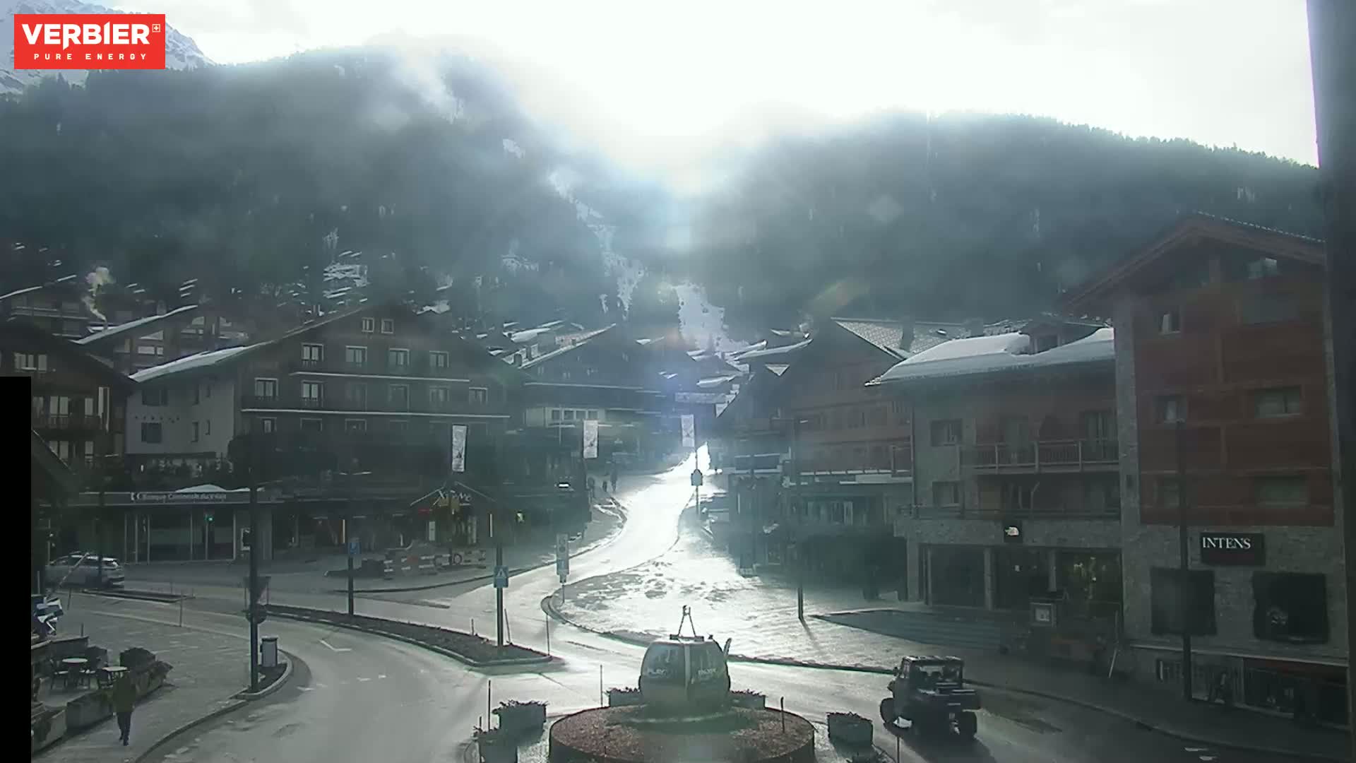 A mostly clear, hazy day reveals a snow-dusted village nestled in a valley between mountains.