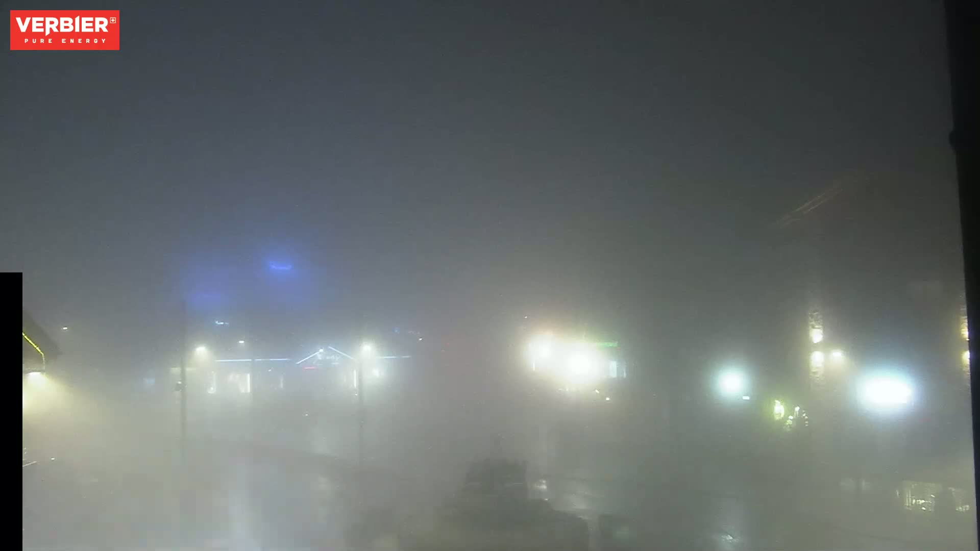 A foggy night scene shows dimly lit buildings and streetlights obscured by heavy fog.