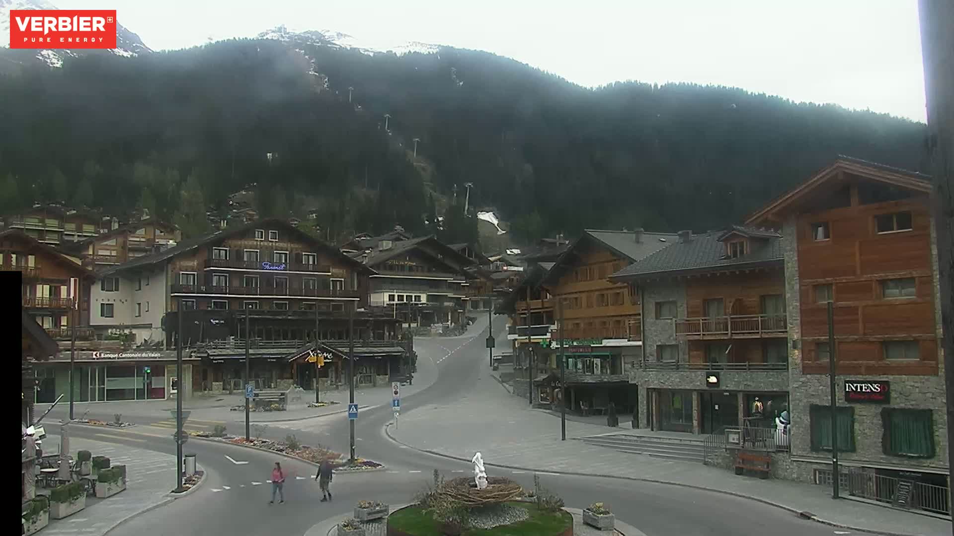 A mostly overcast view of a town nestled in a valley surrounded by a mountain range with ski lifts visible.