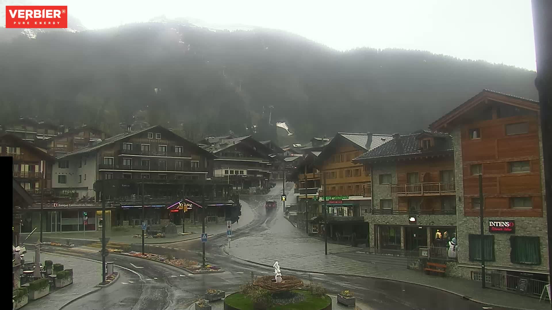 A mountain village street is flooded with rainwater under a heavy, overcast sky.