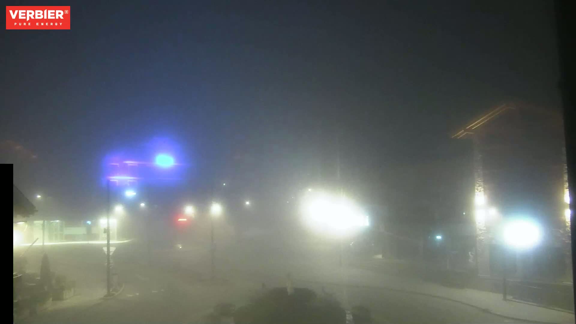 A foggy night scene shows a street with dim lights and buildings barely visible in the heavy mist.