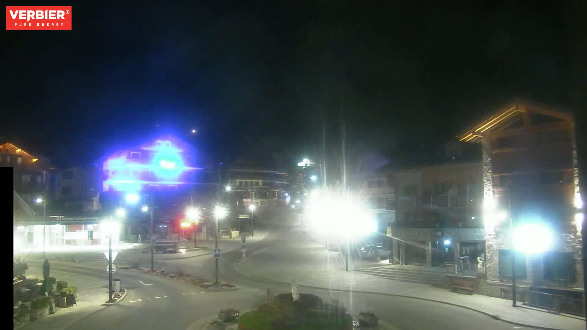 A nighttime view of a town square with illuminated buildings and streets, under a clear sky.