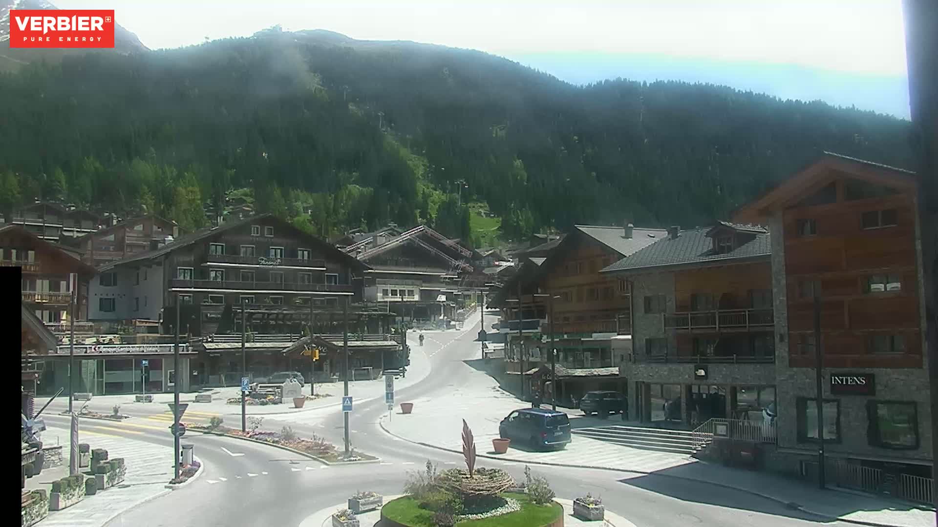 A sunny view of a village nestled in a valley surrounded by green mountains.