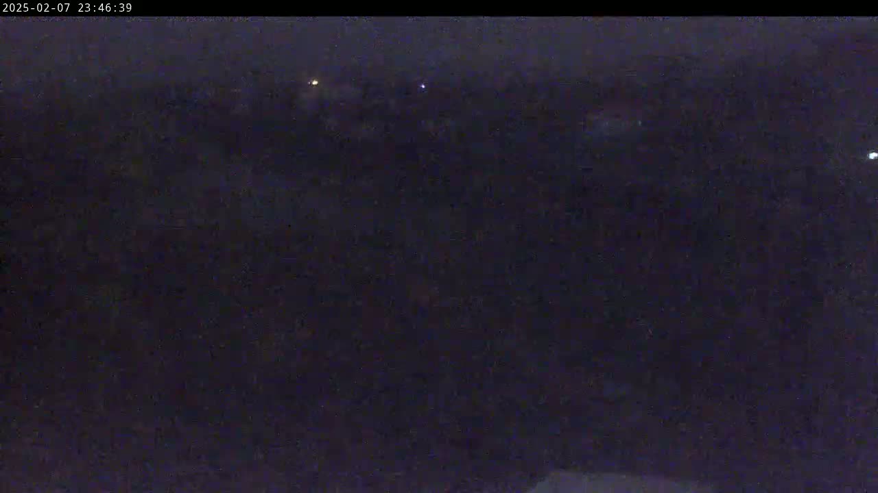A dark, nighttime view of a landscape with a few distant lights visible.