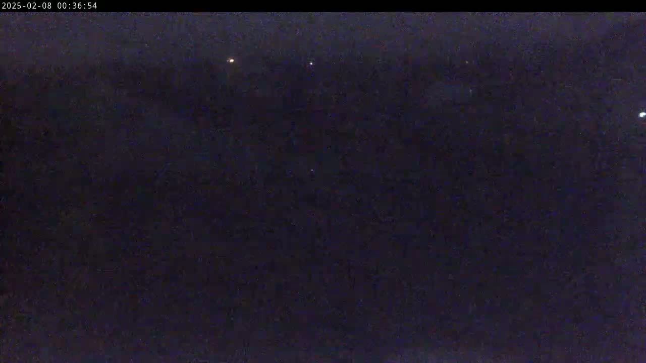 A dark, nighttime outdoor scene shows a few faint lights in the distance under a mostly clear sky.