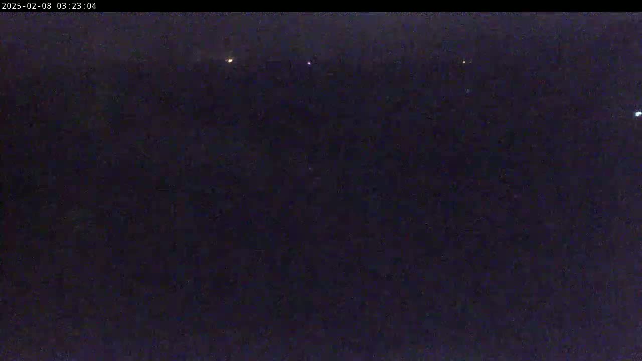 A dark, nighttime scene shows a few distant lights in the hazy darkness.