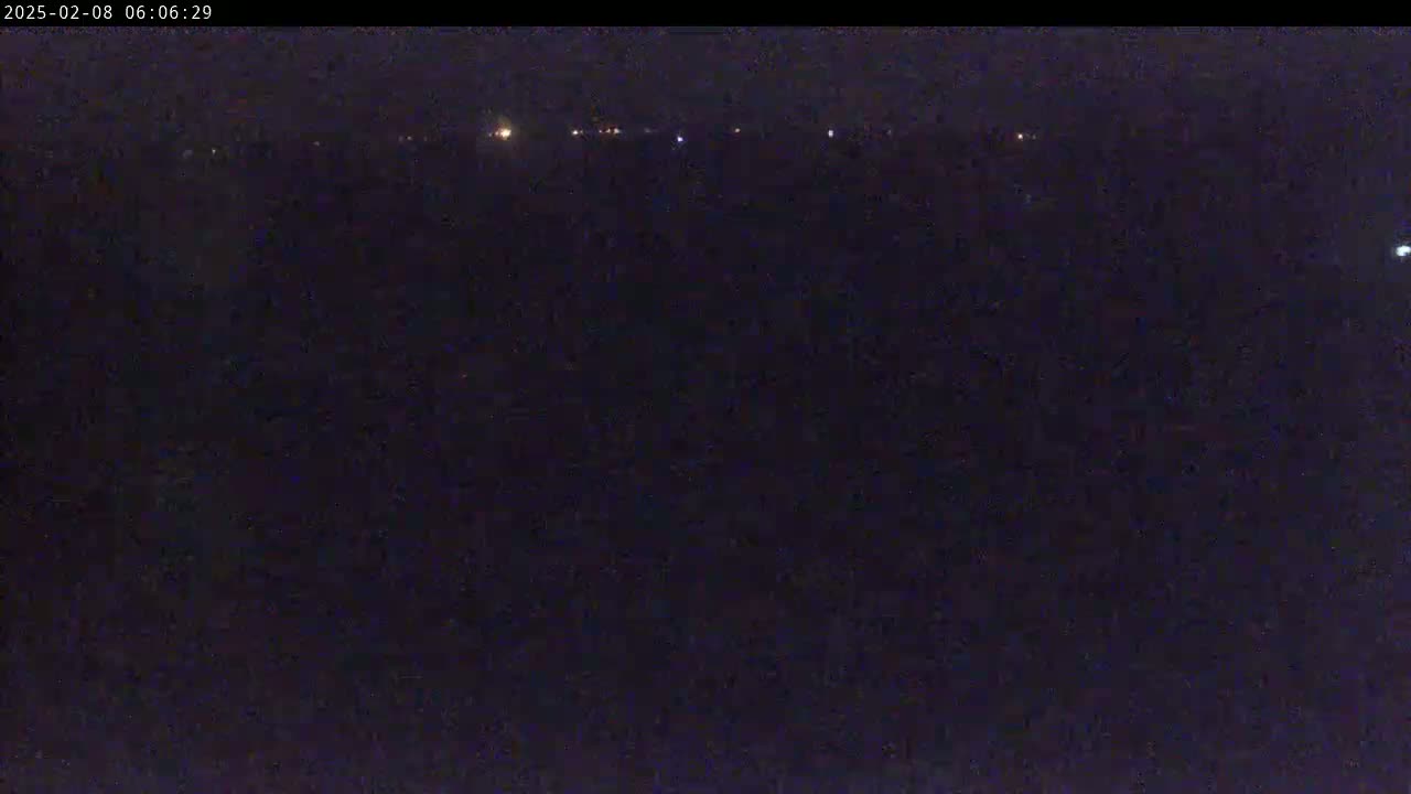 A dark, nighttime scene shows a distant line of faint lights against a mostly black background.