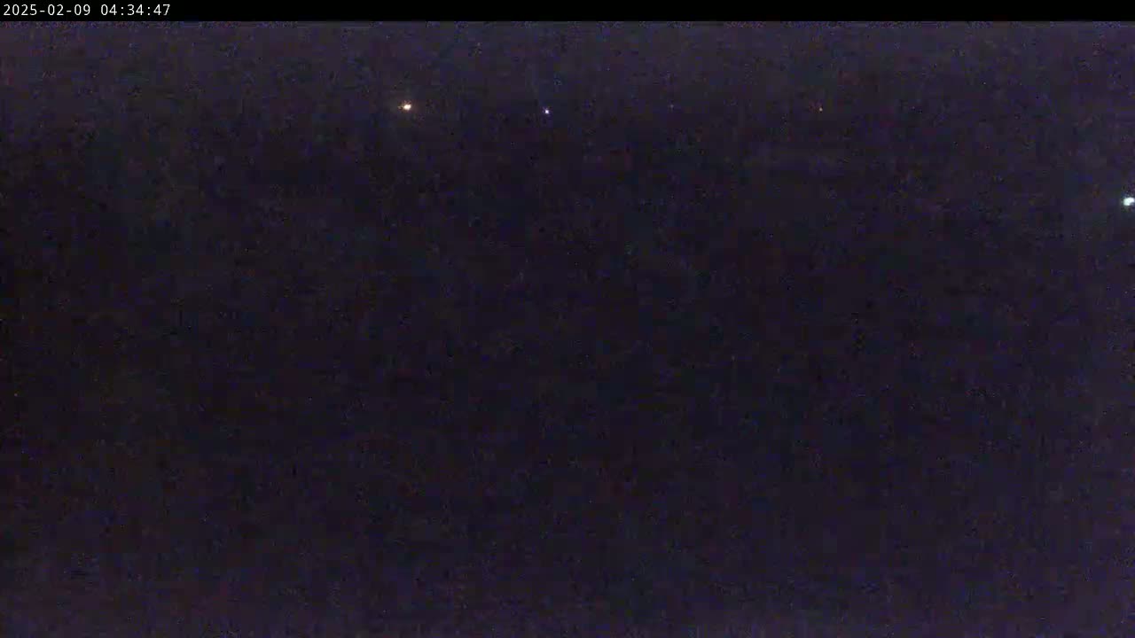 A dark, nighttime scene shows a few faint lights in the distance under a clear sky.