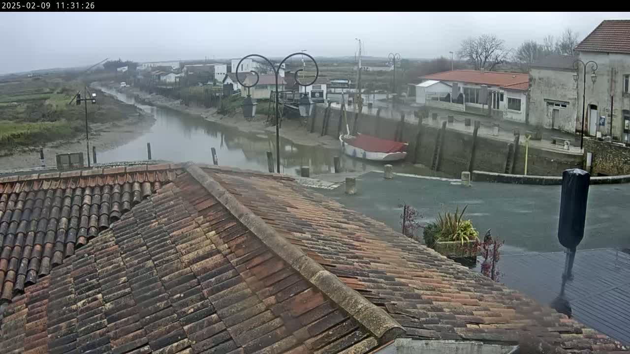 A view from a tiled roof shows a calm waterway passing through a village under an overcast sky.