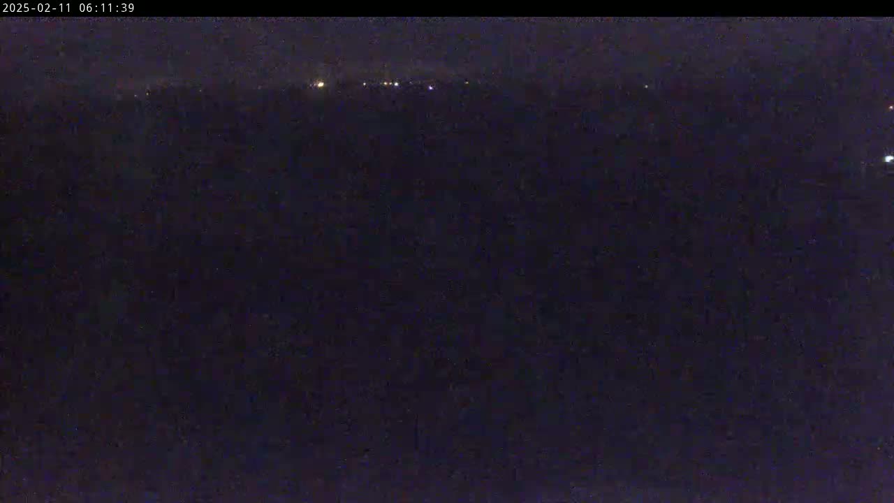 A dark, nighttime scene shows a distant line of faint lights against a mostly black background.
