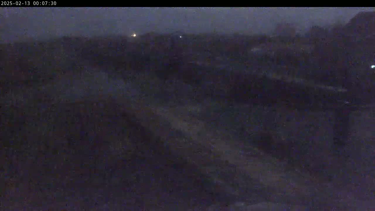 A dark, nighttime outdoor scene shows a blurry view of what appears to be a flat, undeveloped land under a dim, overcast sky.