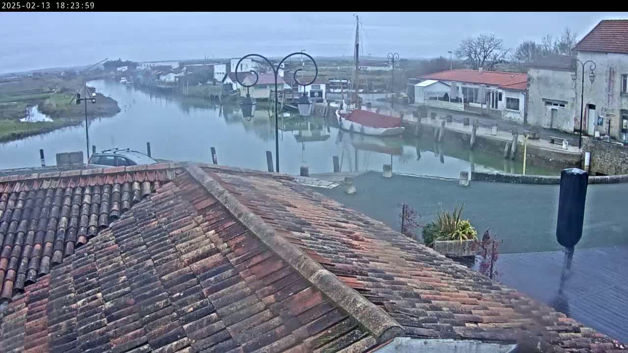A view from a tiled roof overlooks a calm waterway with several boats and buildings on a foggy day.
