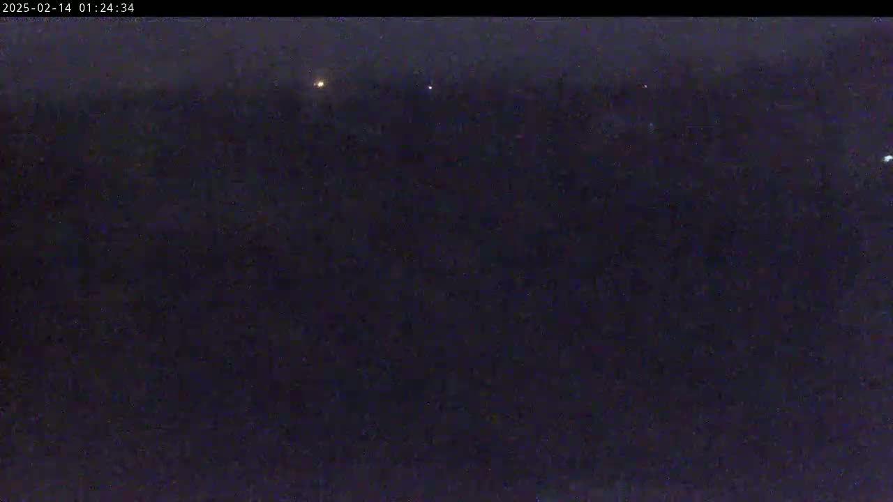 A dark, nighttime scene shows a few faint lights in the distance under a cloudy sky.