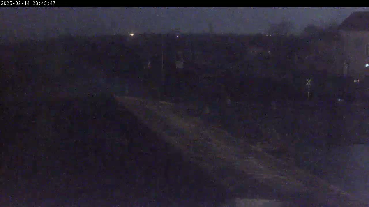 A dark, nighttime view shows a mostly obscured landscape with a few distant lights and a building in the upper right corner.