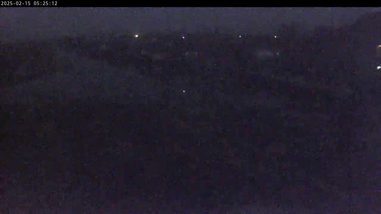 A dark, nighttime view of a sparsely lit landscape under a mostly cloudy sky.