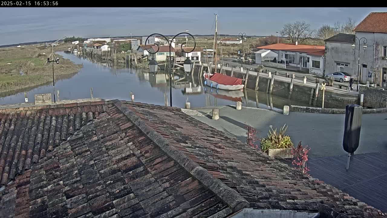 A view from a tiled rooftop shows a calm waterway lined with buildings and boats under a mostly sunny sky.