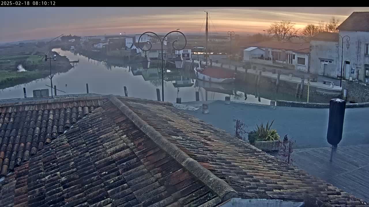 A tiled roof overlooks a calm canal at sunrise, with boats moored along the waterfront and buildings lining the edge.
