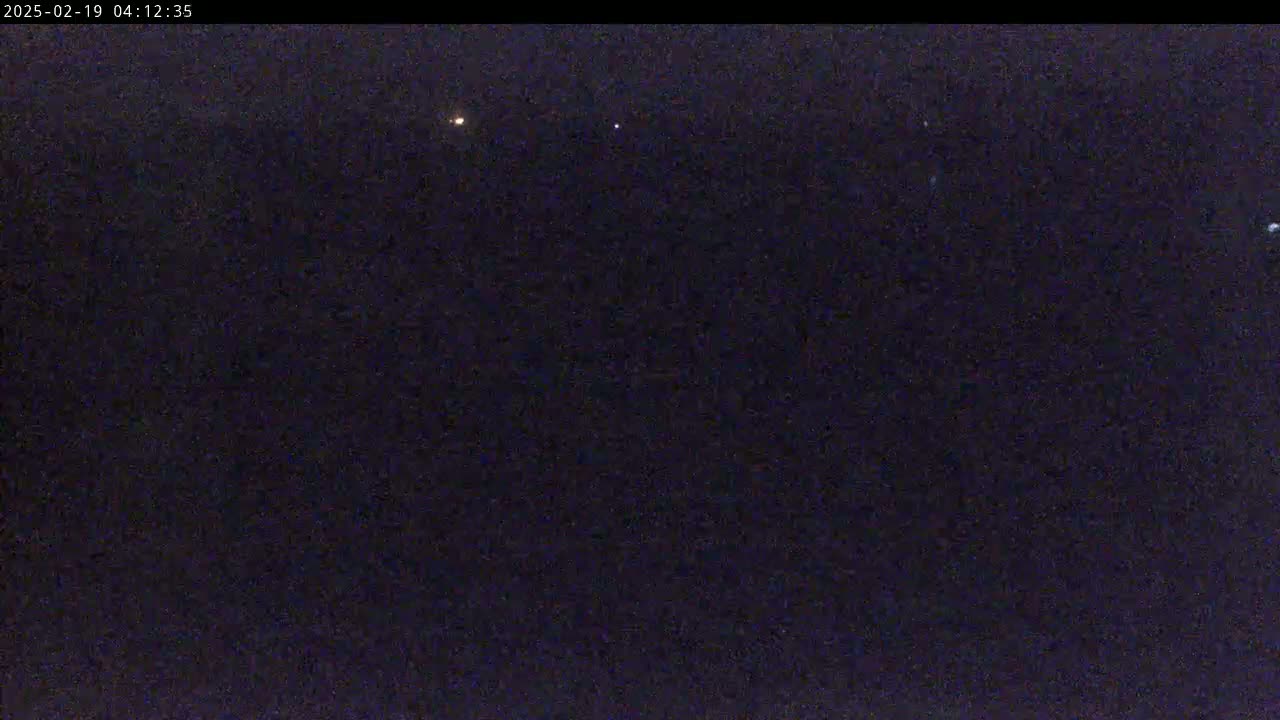 A dark, nighttime scene shows a few faint lights in the distance under a clear, dark sky.