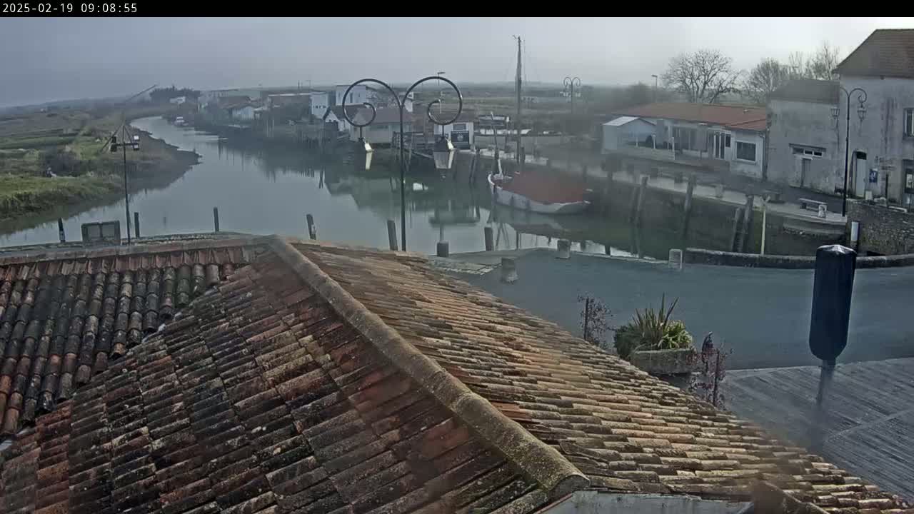 A view from a tiled roof overlooks a calm waterway with boats docked near buildings in a hazy atmosphere.
