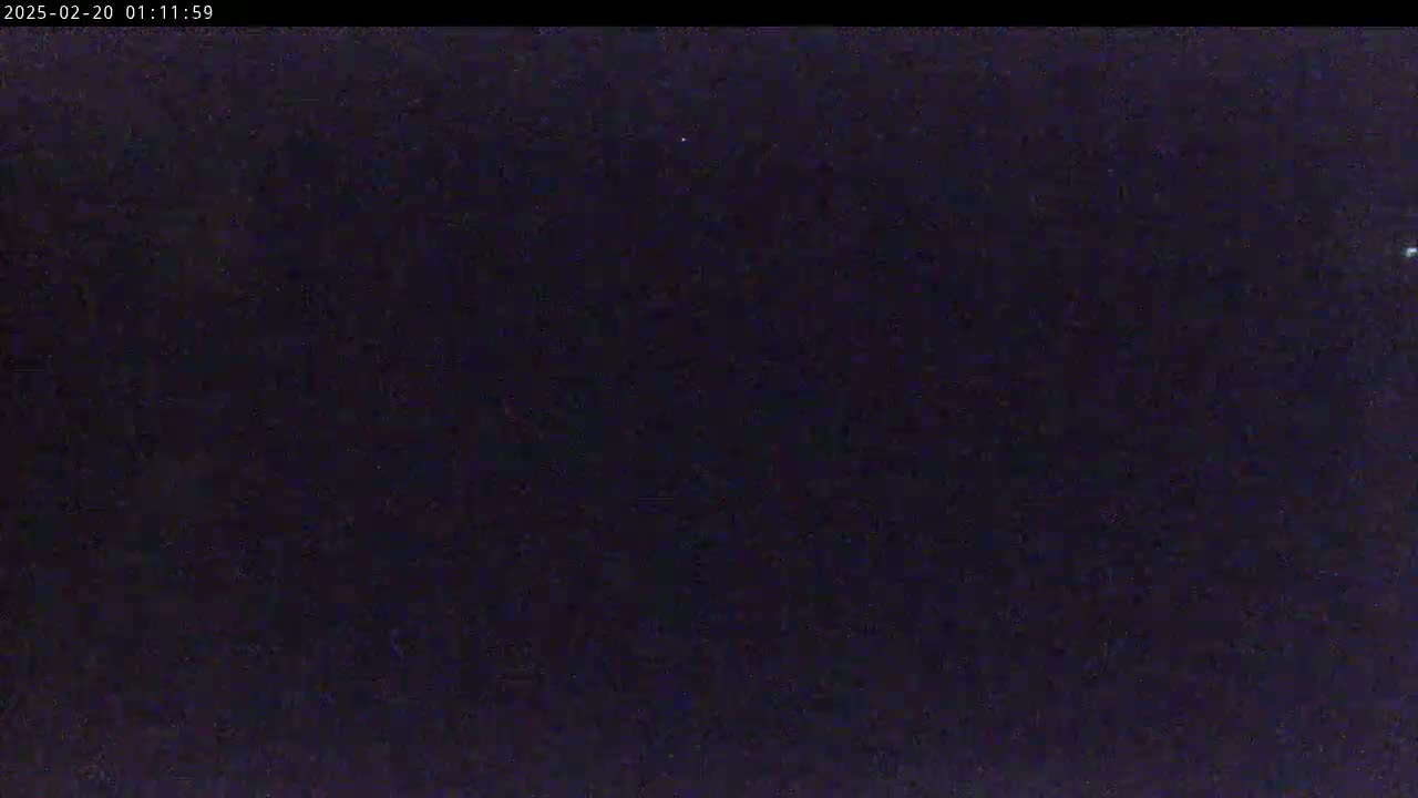 A dark, nighttime scene shows a mostly clear sky with a few faint lights visible.