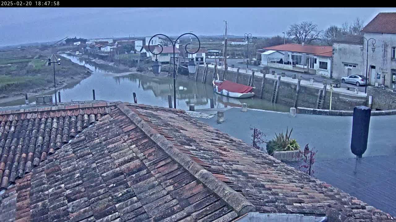 Overlooking a calm canal, a boat is moored near buildings under an overcast sky.